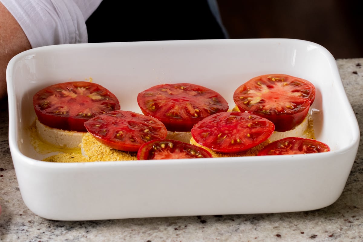 adding tomato slices to the stacks in the baking pan