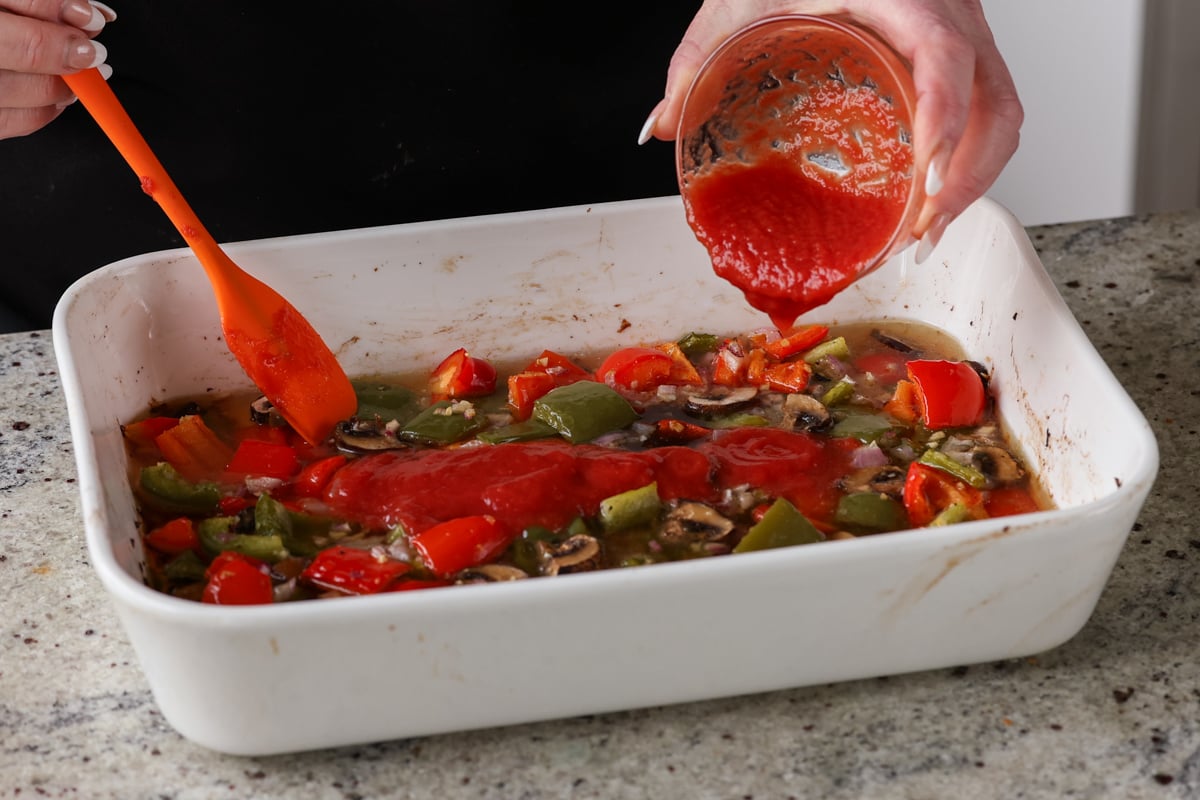 adding tomato puree to the pan of baked veggies