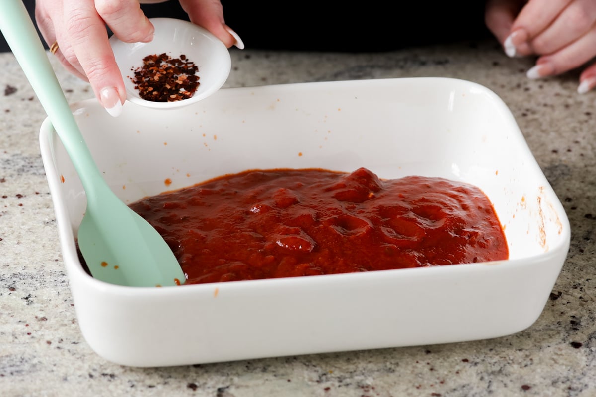 adding seasoning to the pasta sauce in the baking pan