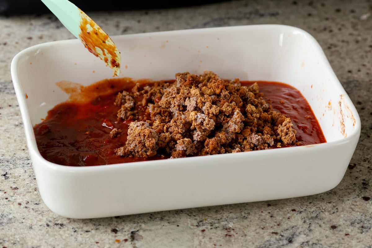 adding vegan ground beef to the pasta sauce in the baking pan
