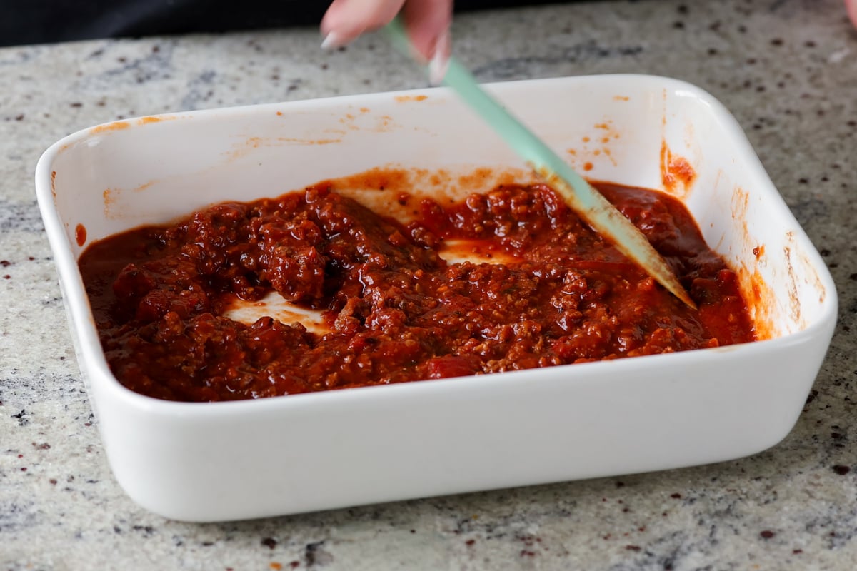 mixing and spreading the pasta sauce in the baking pan
