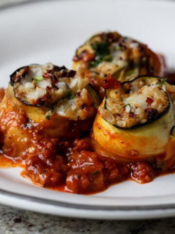 zucchini rolls on a white plate with tomato sauce