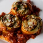 zucchini rolls on a white plate with tomato sauce