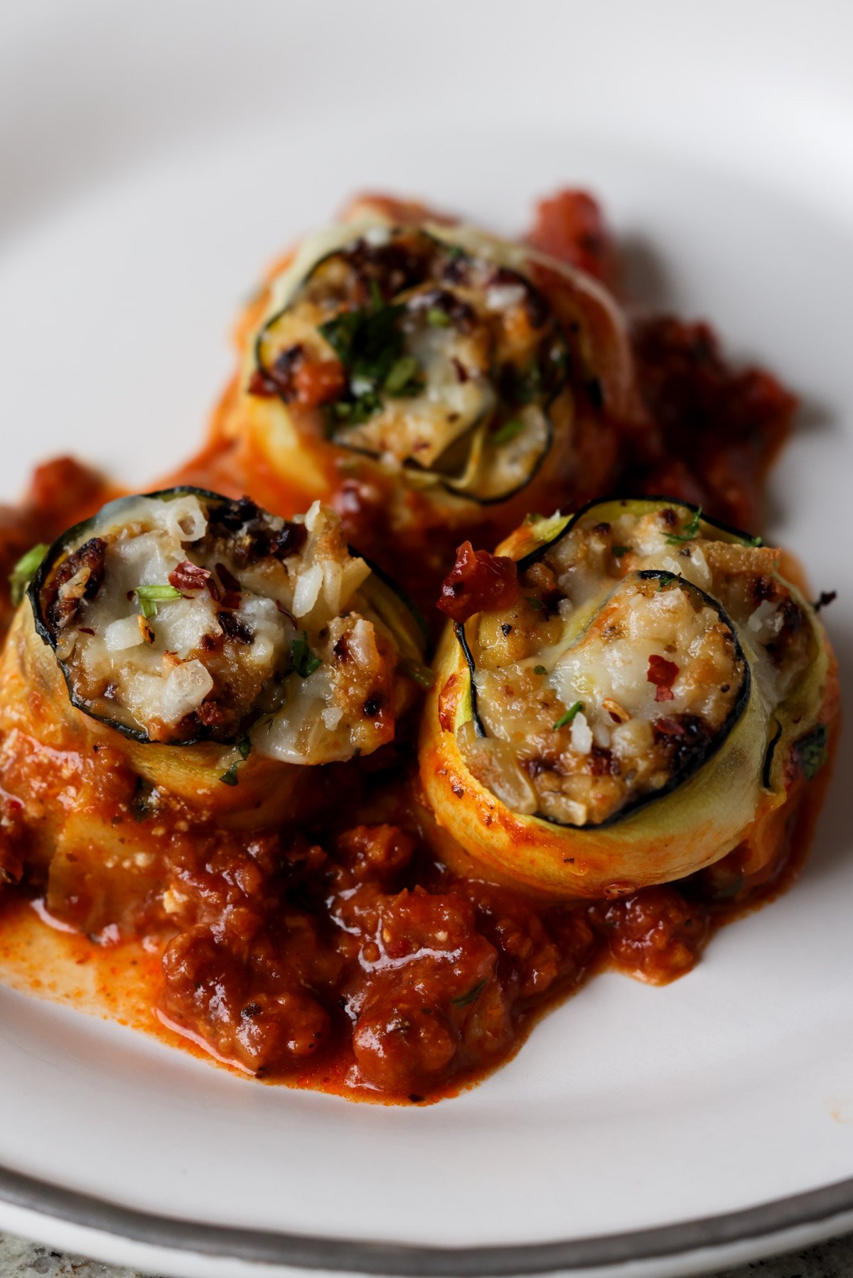 zucchini rolls on a white plate with tomato sauce
